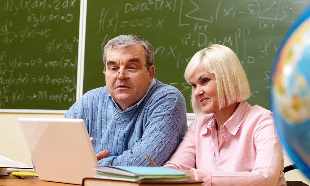 Portrait of mature man and aged female working with laptop in classroom