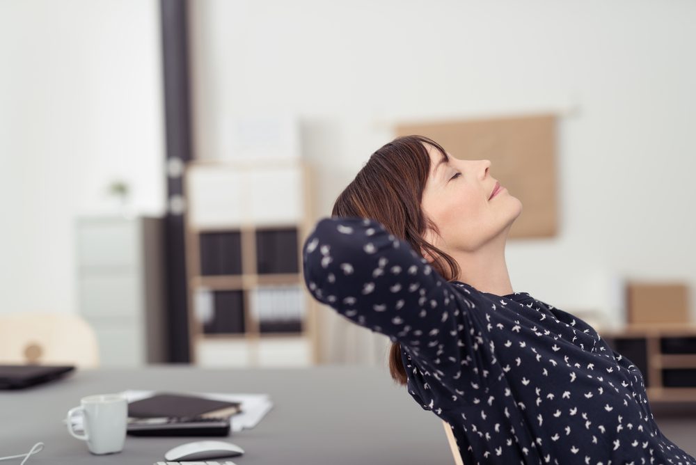 Tired office woman at her worktable, leaning her back on a chair with hands at the back of her head and eyes closed, emphasising of thinking something
