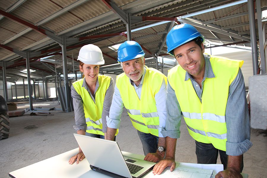 Three happy manufacturing employees wearing hi vis vests and helmets